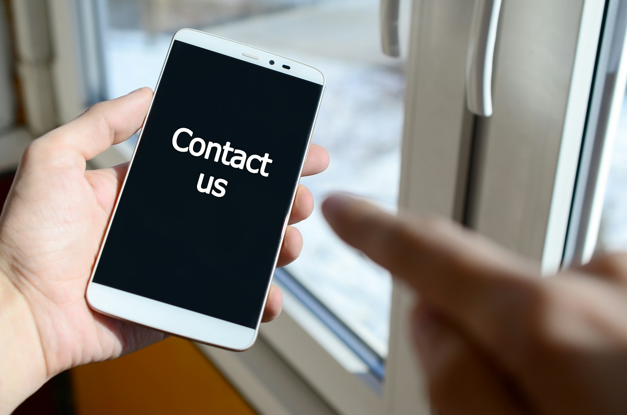 A person sees a white inscription on a black smartphone display that holds in his hand. Contact us