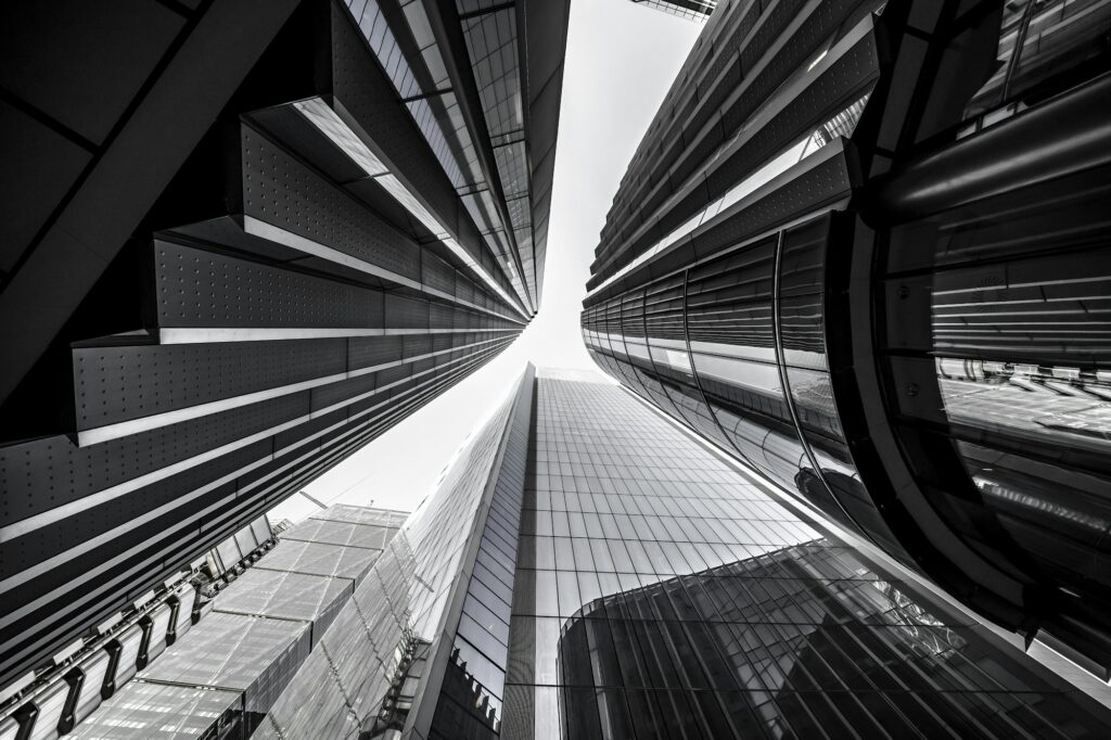 Low angle greyscale of modern skyscrapers with glass windows under sunlight